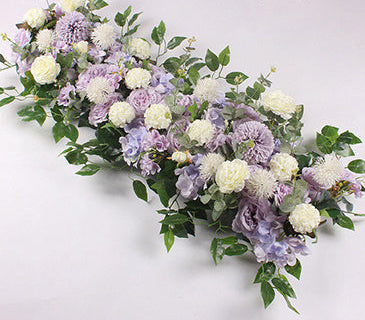 Light purple and white floral arrangement with green leaves on a light gray background