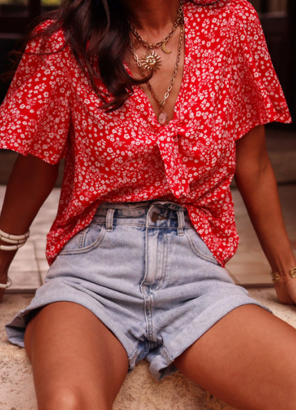 Person wearing a red floral blouse and denim shorts sitting on a couch.