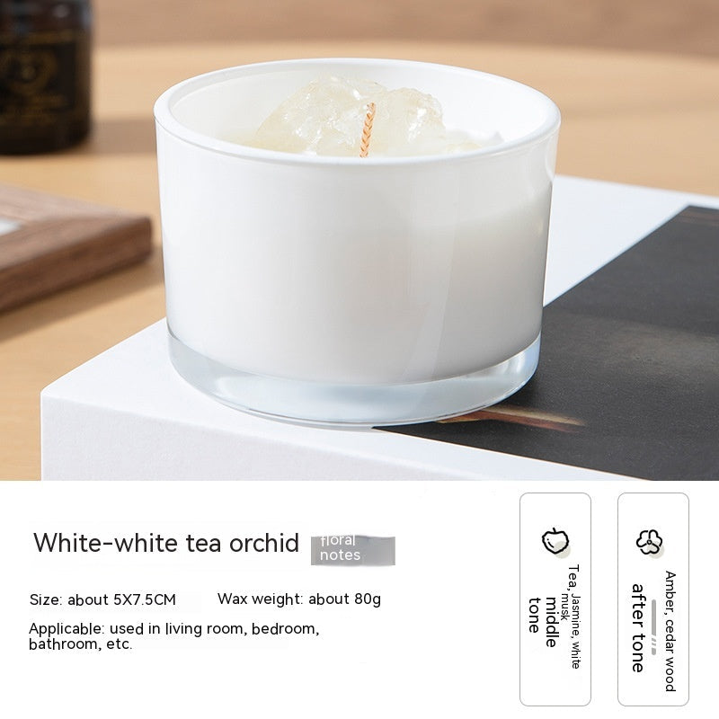 White candle in a glass container on a wooden surface with product details below.