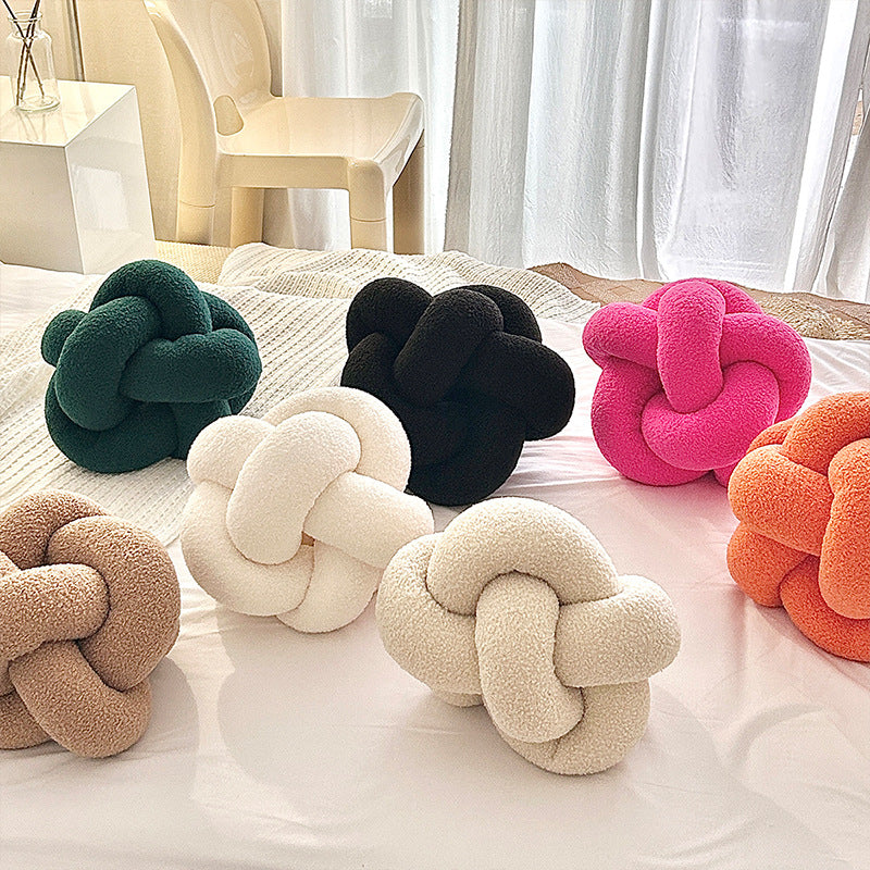 Colorful knot-shaped cushions on a bed with a neutral background