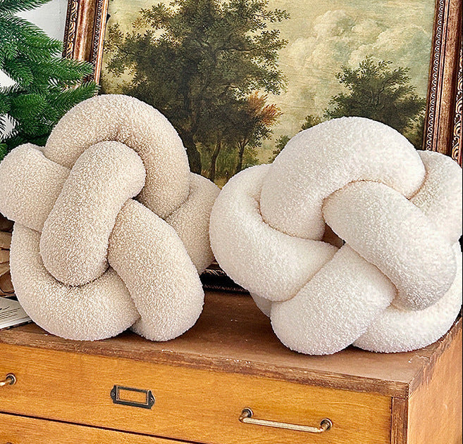 Decorative knot pillows on a wooden dresser with a Christmas tree and painting in the background.