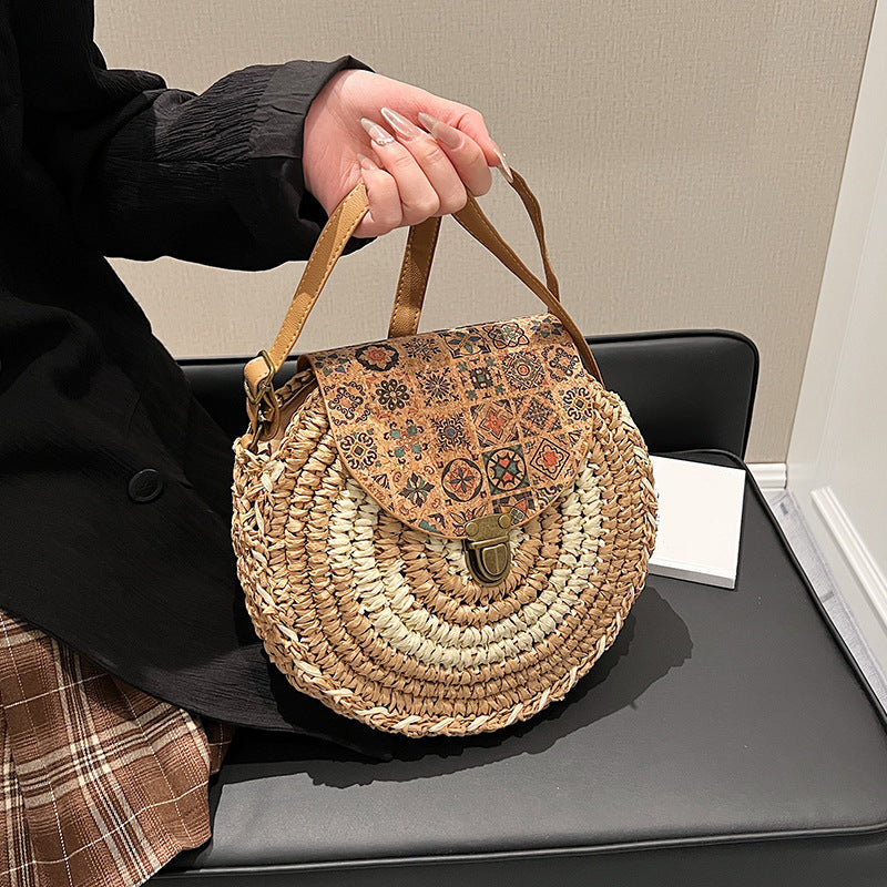 Person holding a round woven bag with a patterned flap on a desk.