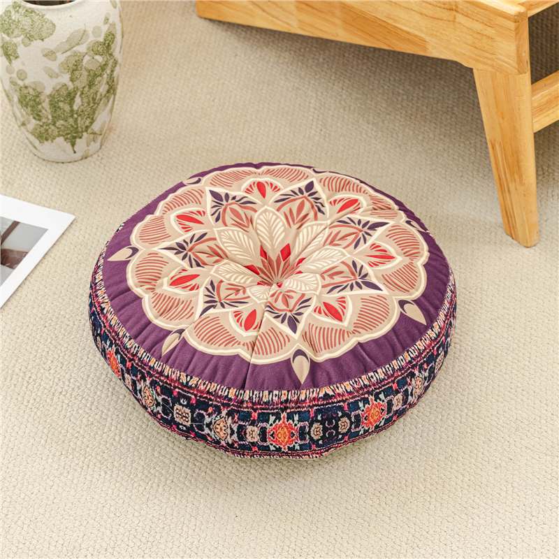 Round floral cushion on a beige carpet with a wooden table corner.