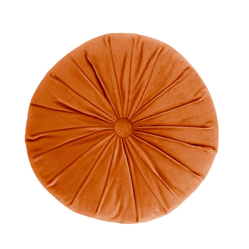 Round orange pillow with pleated texture on a white background