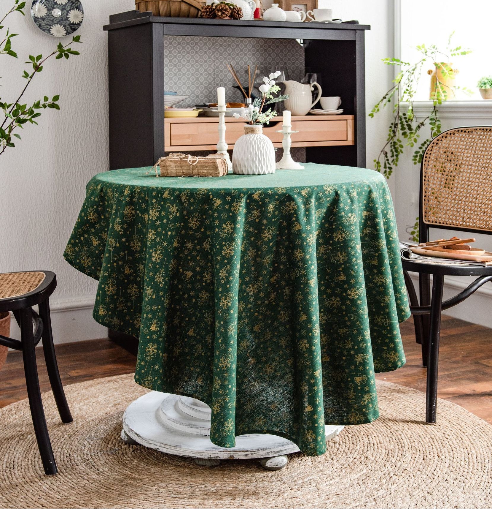 Round table with a green patterned tablecloth in a room with a chair and decorative items.