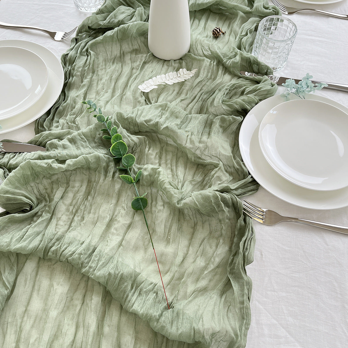 Table setting with a green textured tablecloth, white plates, and silverware.