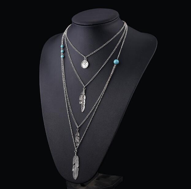Layered silver necklace with turquoise beads on a black mannequin bust.