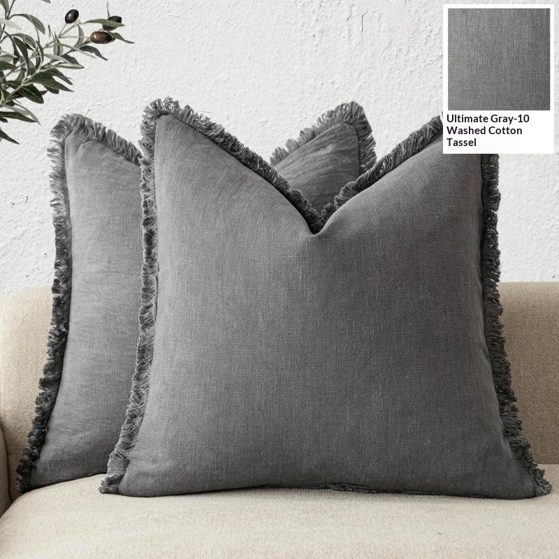 Gray pillows with tassels on a beige sofa against a light gray wall.