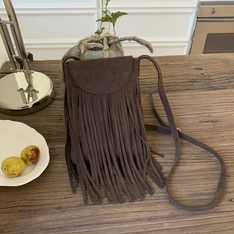 Brown suede handbag with fringe on a wooden surface