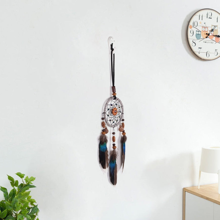 Dreamcatcher with feathers hanging on a white wall next to a clock.