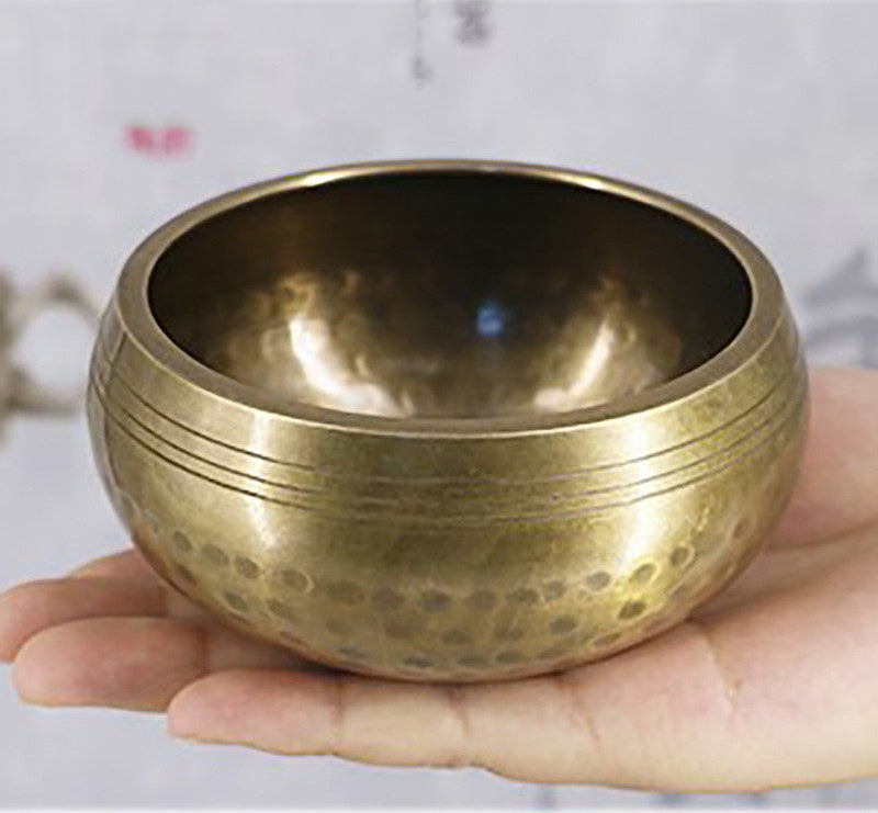Bronze singing bowl held in a hand with a blurred background