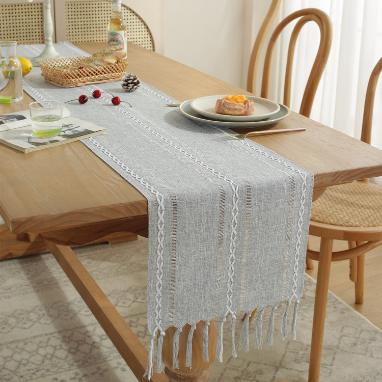 Dining table with a gray table runner, plates, and glasses on a wooden floor.