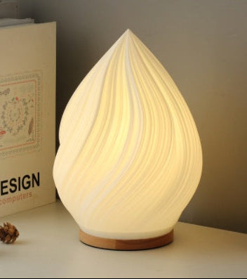 Teardrop-shaped lamp emitting a warm glow on a surface with books and pine cones.