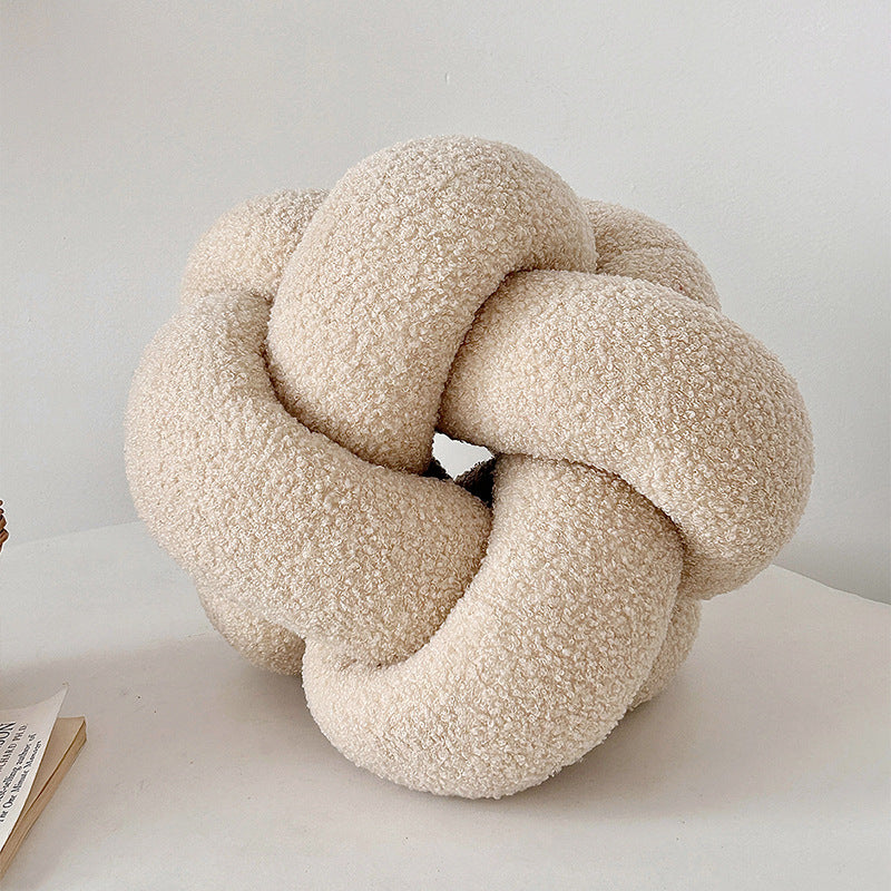 Textured knot pillow on a white surface with a light gray background