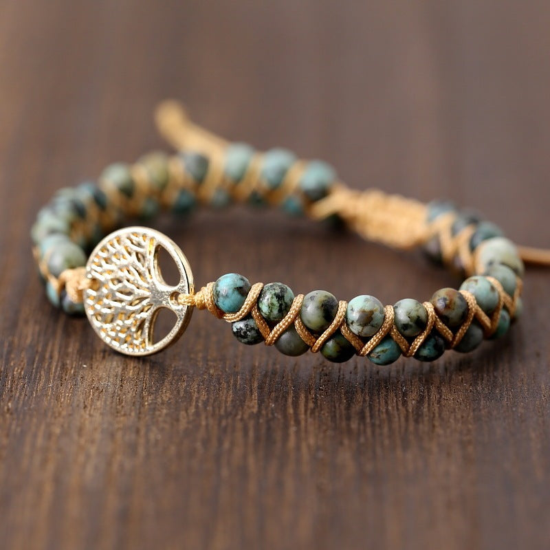 Bracelet with green beads and gold tree of life charm on a wooden surface