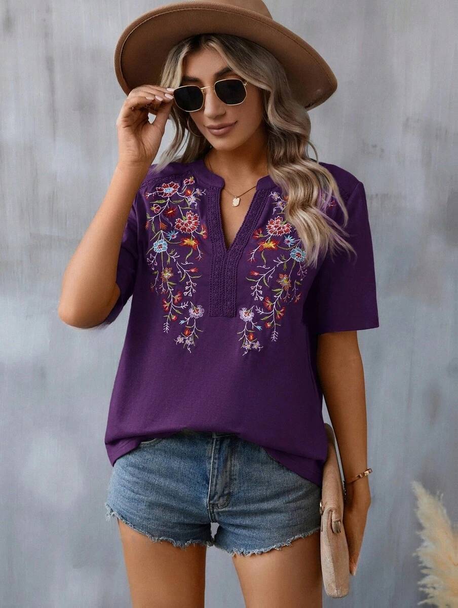 Woman wearing a purple embroidered top and denim shorts against a gray background