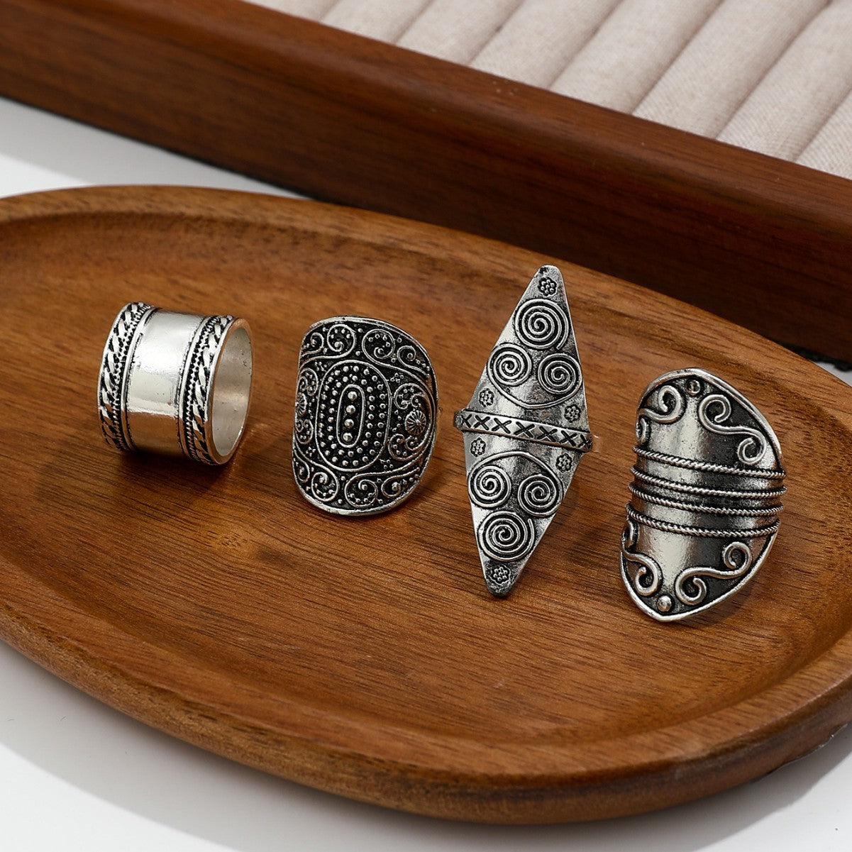 Four silver rings with intricate designs on a wooden tray.