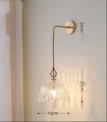Wall-mounted lamp with crystal shade and gold fixture on a white wall.