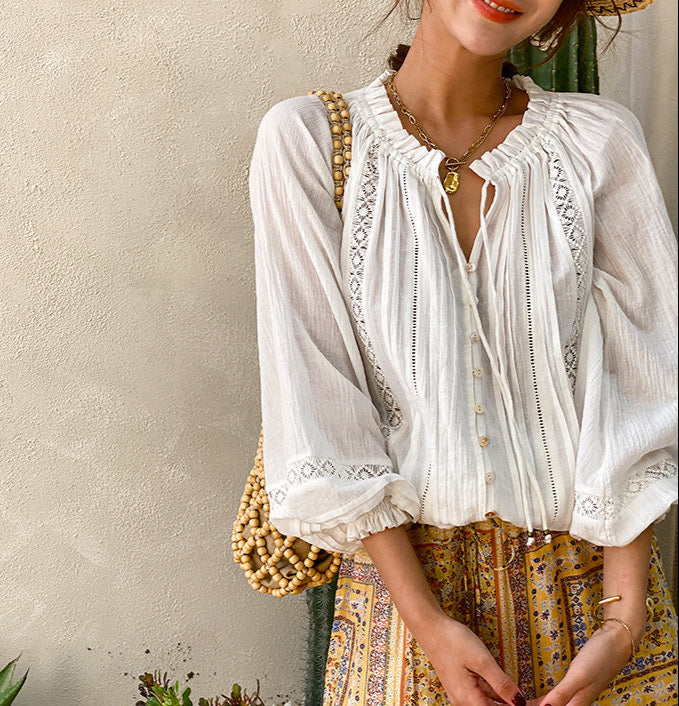 Woman wearing a white blouse with intricate details and a patterned skirt against a neutral wall.
