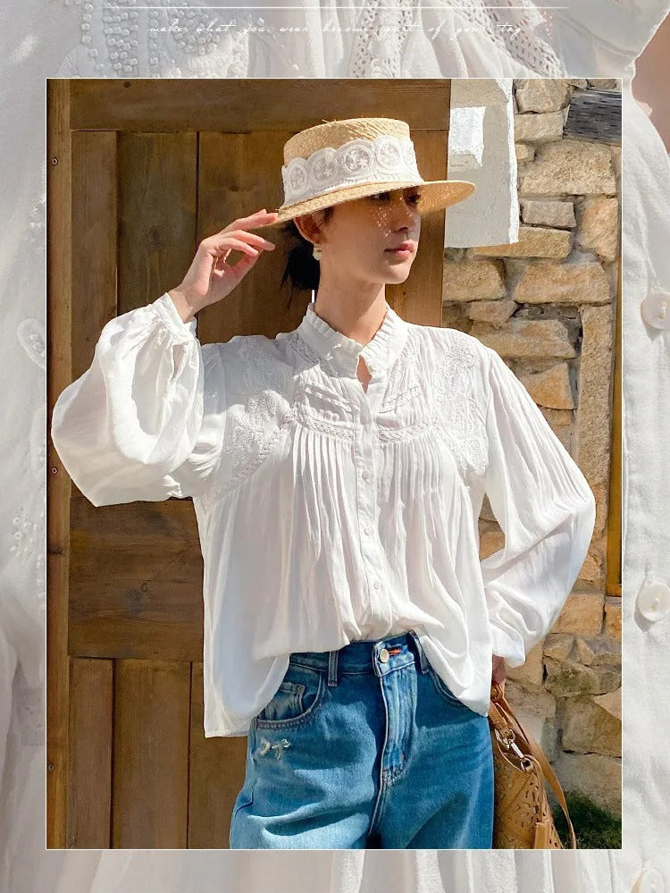 Woman wearing a white blouse and straw hat with lace details, standing against a stone wall.
