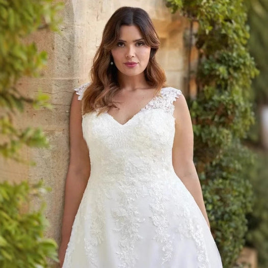 Woman in a white lace dress standing against a stone wall with greenery.