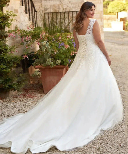 Woman in a white wedding dress standing outdoors with plants and a stone wall in the background
