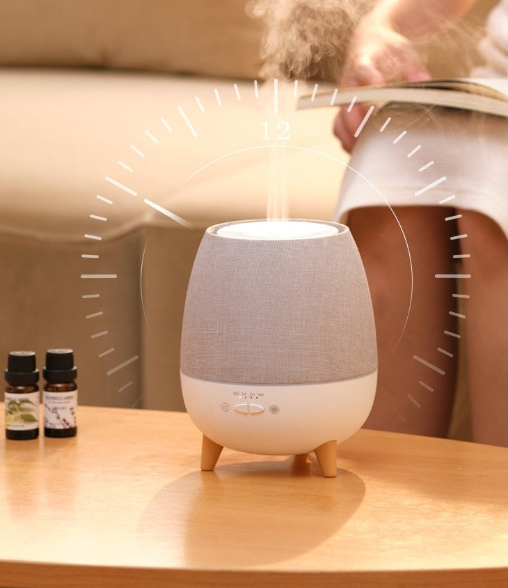 White and gray diffuser on a wooden surface with steam rising, person reading in the background.