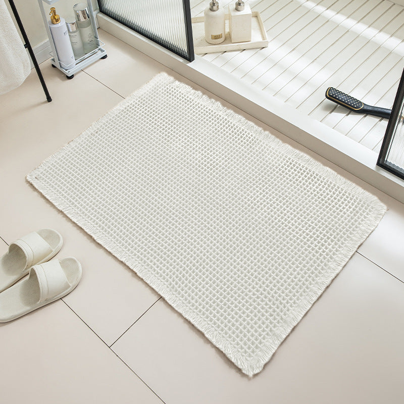 White textured bath mat on a tiled bathroom floor with slippers and a mirror in the background.