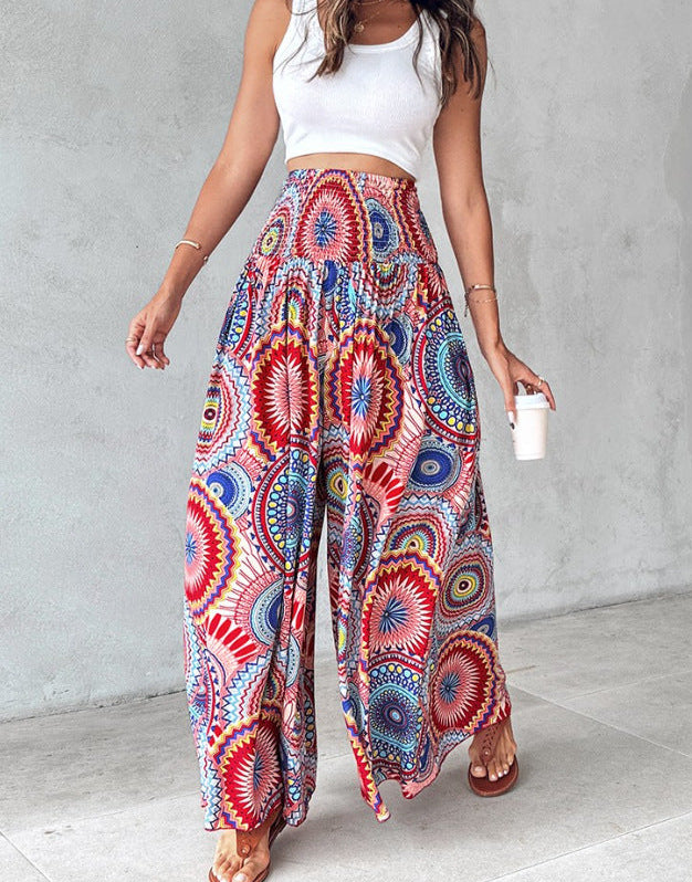 Woman wearing a white top and colorful patterned pants against a gray wall.
