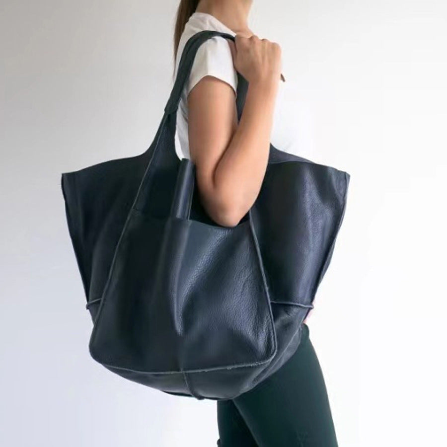 Person holding a dark blue leather tote bag against a plain background