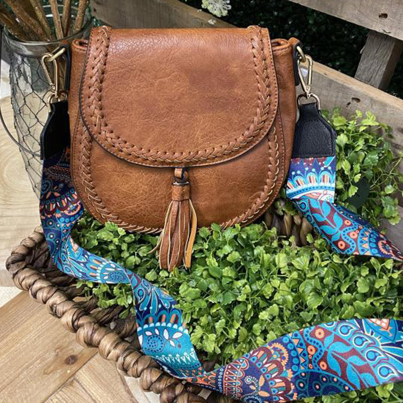 Brown leather bag with a colorful strap on a wooden surface