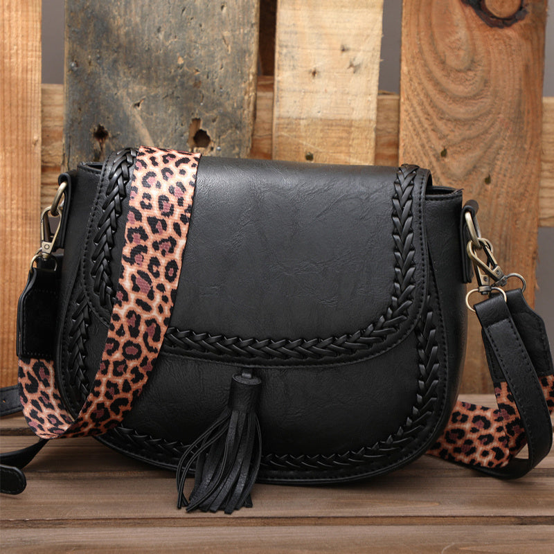 Black leather handbag with a braided strap and leopard print accents on a wooden surface.