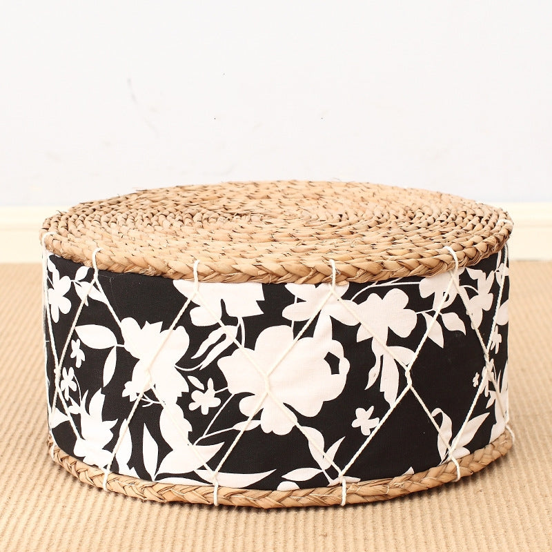 Round woven ottoman with black floral pattern and natural woven top on a beige surface.