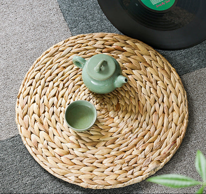 Woven mat with a green teapot and cup on a gray surface next to a black vinyl record.