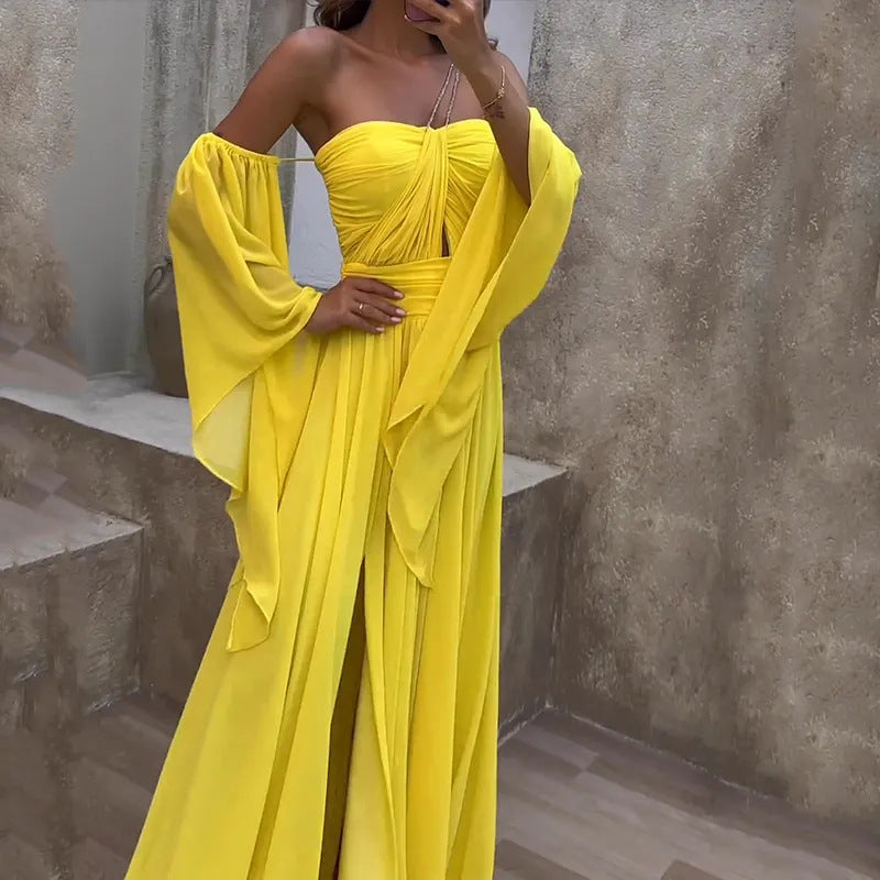 Woman wearing a yellow dress with wide sleeves against a textured wall.
