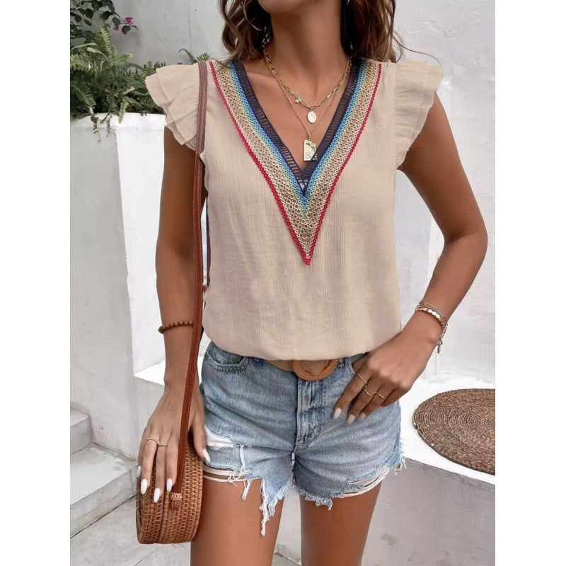 Woman wearing a beige top with colorful neckline and denim shorts, holding a brown bag.