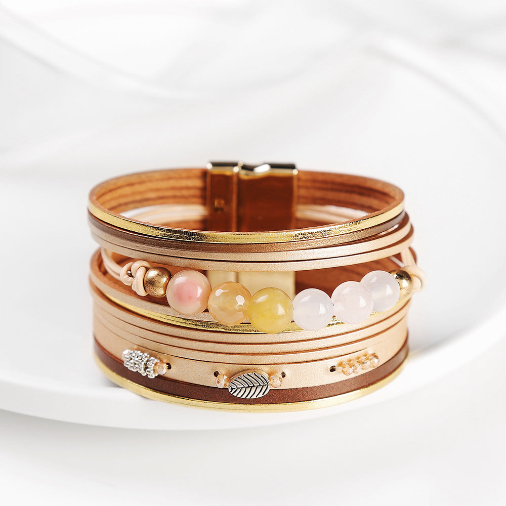 Stack of gold and brown bracelets with beads and leaf charms on a white background