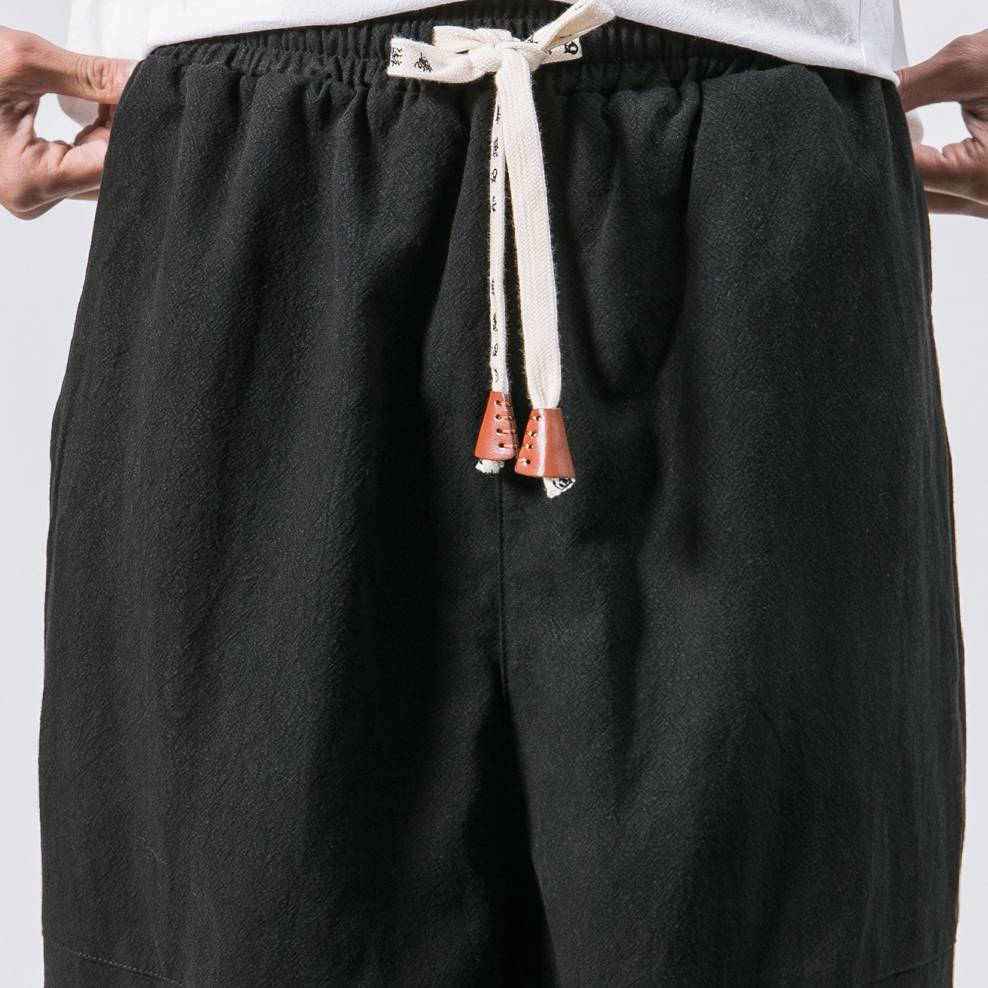 Black pants with a drawstring and orange buttons on a white background