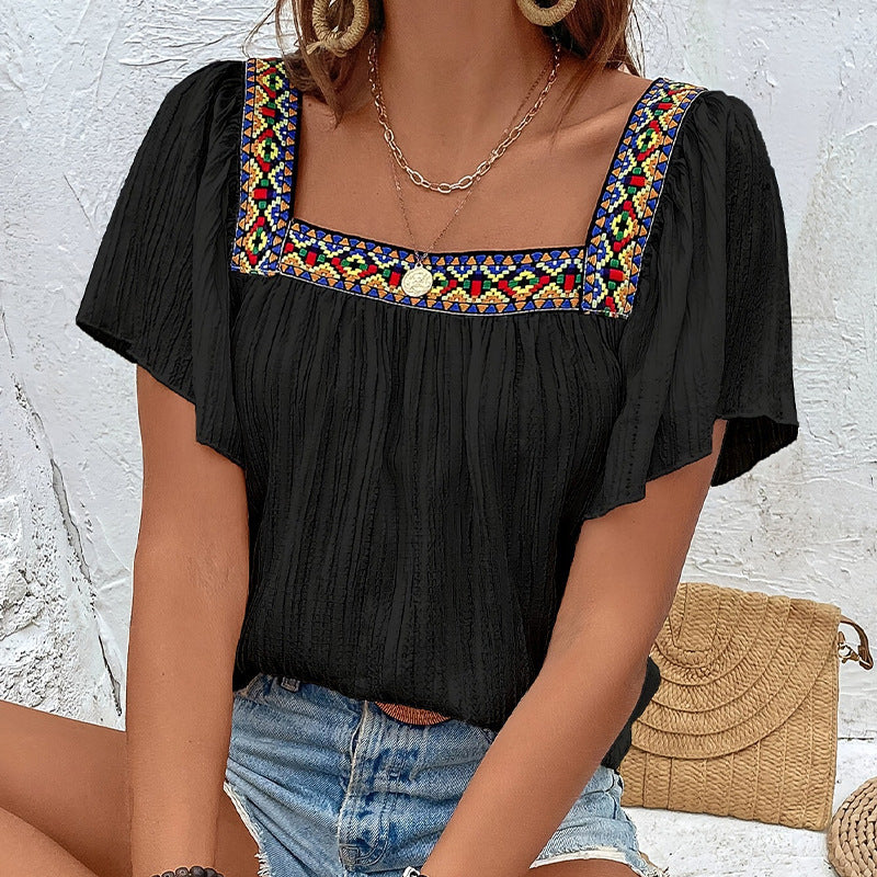 Black top with colorful embroidery on a textured white background