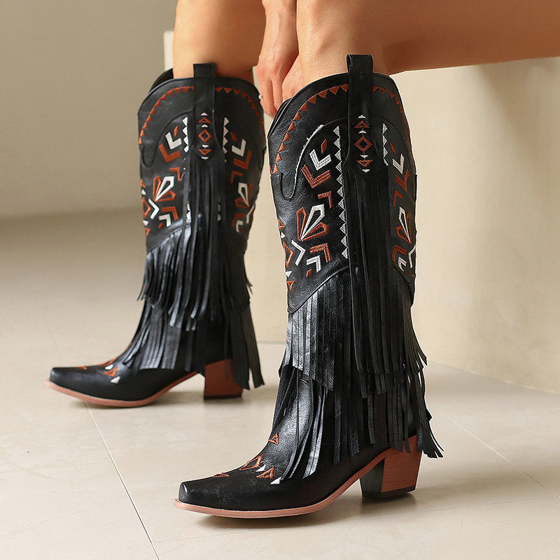 Black fringe cowboy boots with intricate patterns on a neutral background