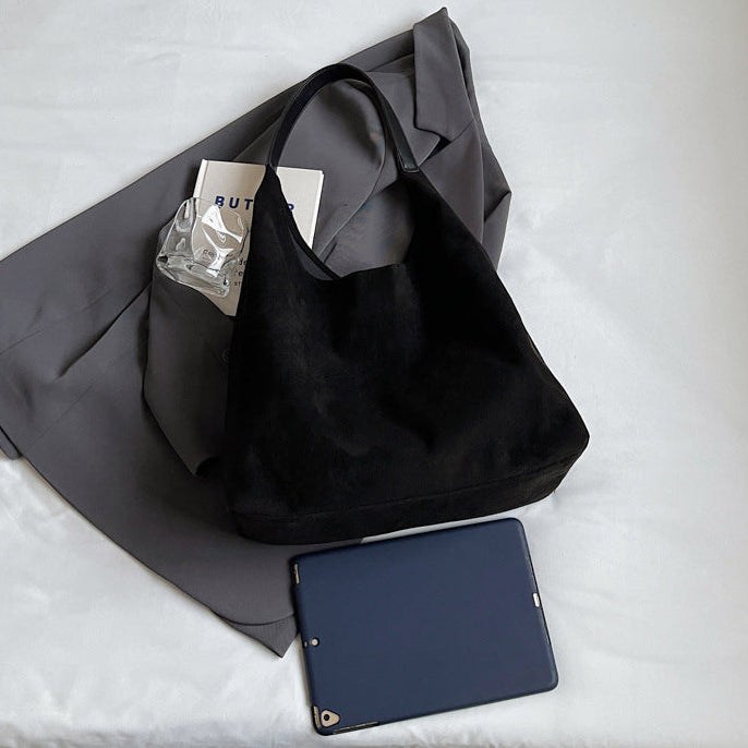 Black tote bag with a gray garment and blue phone on a white surface