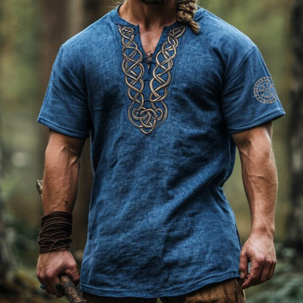 Man wearing a blue t-shirt with intricate designs in a forest setting