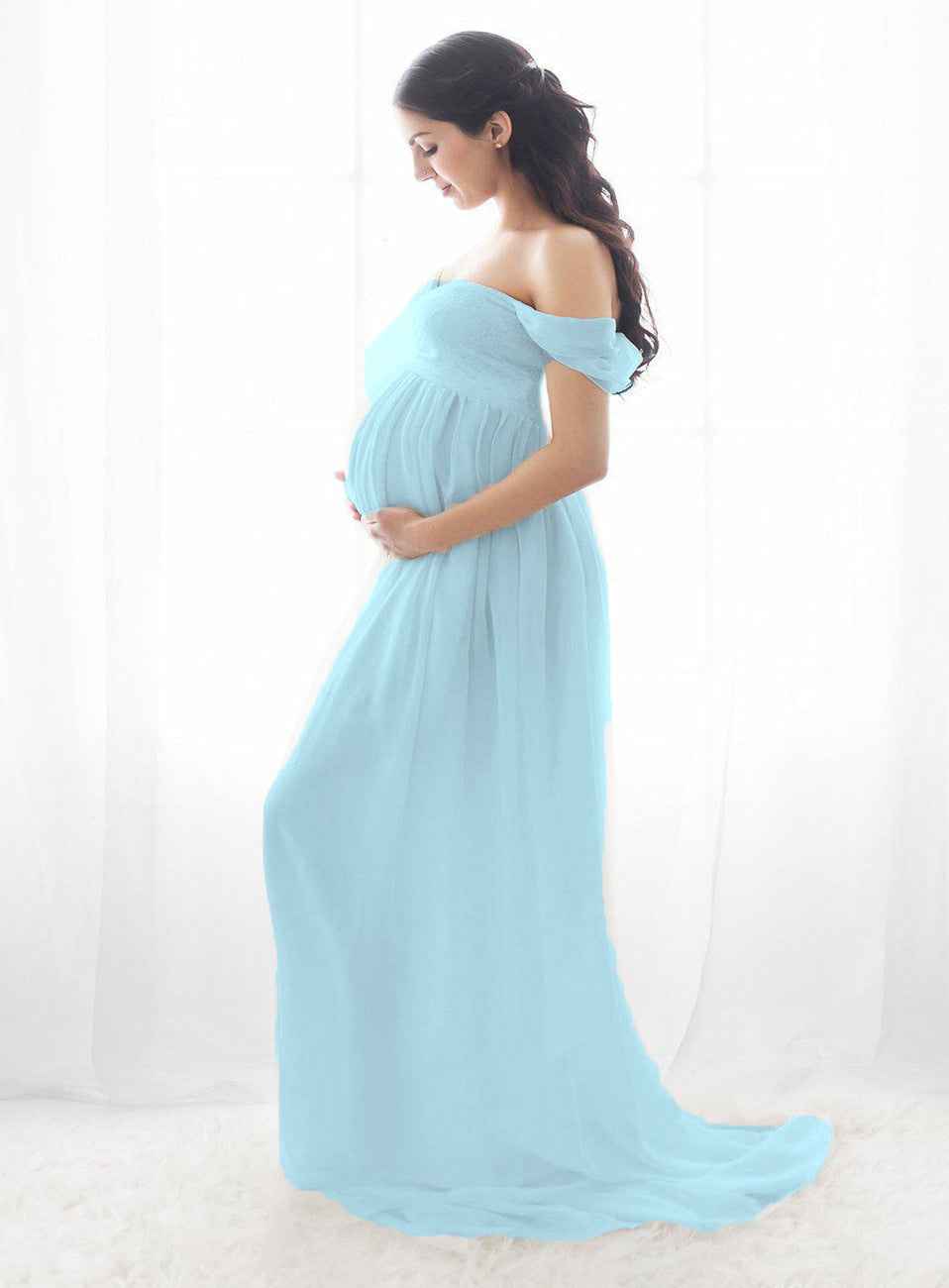 Pregnant woman wearing a light blue off-shoulder dress against a white background