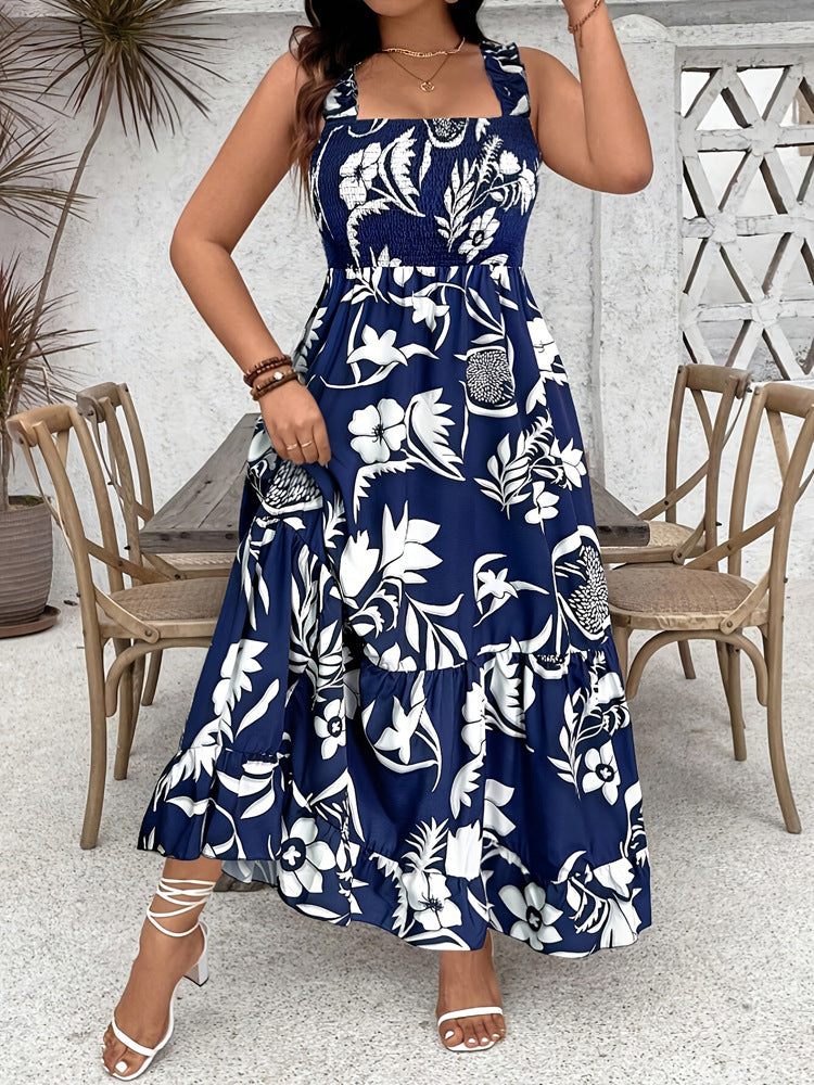 Woman wearing a blue floral dress in an outdoor setting with wooden chairs and a table.