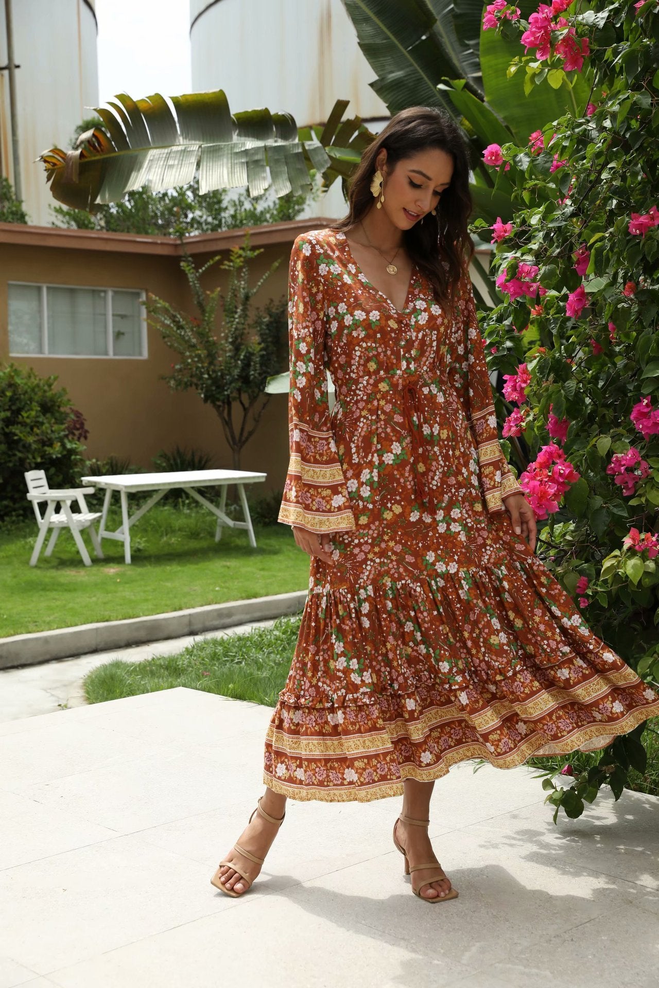 Woman in a floral dress standing outdoors with greenery and a house in the background