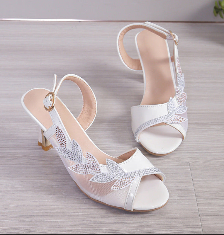 White high-heeled sandals with lace detailing on a wooden surface