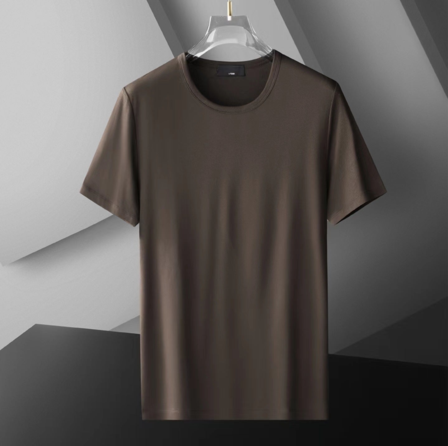 Brown t-shirt on a clear hanger against a gray geometric background