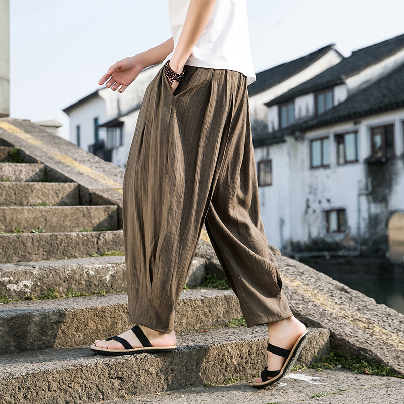 Person wearing brown wide-leg pants and sandals on stone steps with a traditional building in the background.