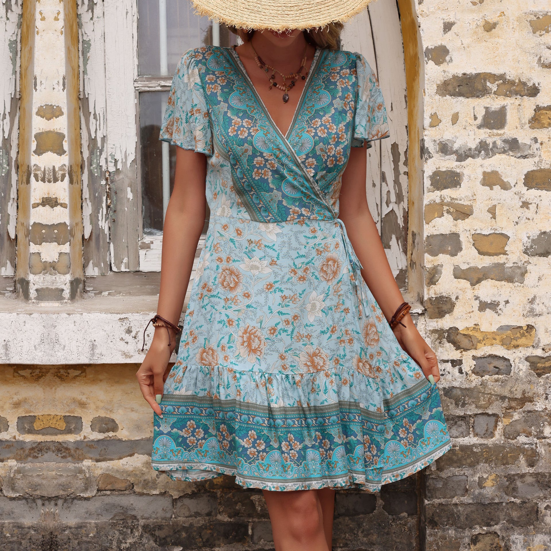 Woman wearing a blue floral dress standing against a stone wall.