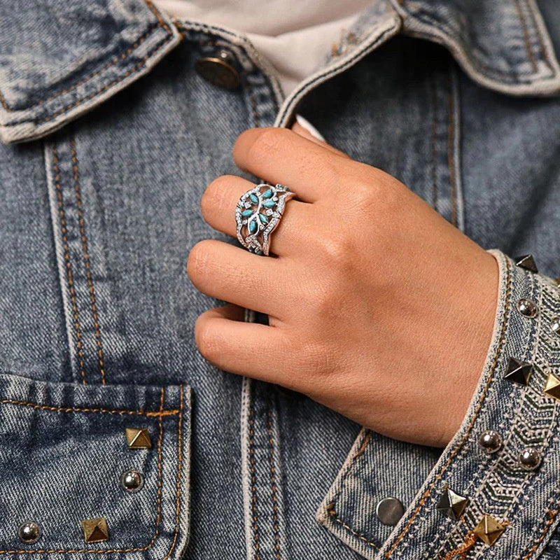 Hand wearing a silver ring with blue gemstones against a denim jacket background